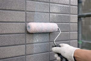 板橋区の現場でタイル外壁にクリヤー塗装を行っている様子。ローラーでクリヤー塗料を塗布し、タイルの質感と目地を保護している施工中の写真