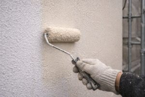板橋区で外壁塗装の中塗り工程として、下塗り後のモルタル外壁に弾性塗料をローラーで塗布している施工中の様子