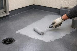 板橋区の住宅ベランダで防水層の状態を確認しながらトップコートを塗り替えている防水工事の施工中の様子