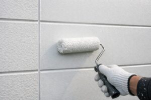外壁に造膜型塗料をローラーで塗り、表面に均一な塗膜を形成している作業の様子