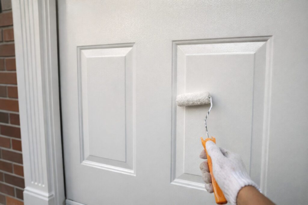 板橋区の住宅で木製玄関ドアをローラーで塗装している様子