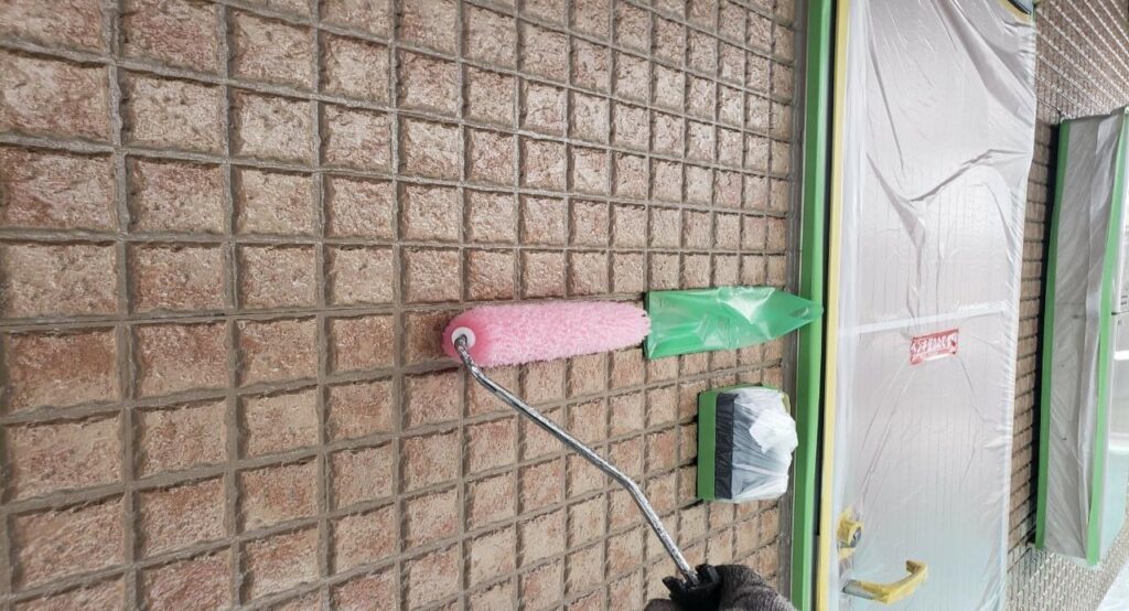 練馬区の集合住宅で、下地処理とシーリング工事完了後に外壁へクリヤー塗料を上塗り1回目でローラー塗布している施工中の様子