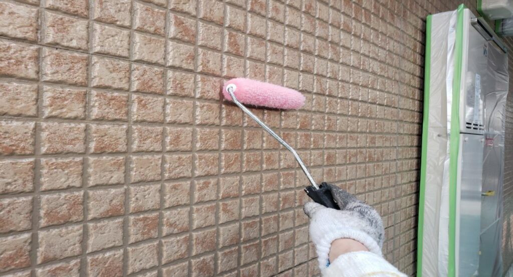 意匠性のある外壁材に対し、塗りムラが出ないようローラー操作を調整しながらクリヤー塗装の上塗り1回目を行っている様子