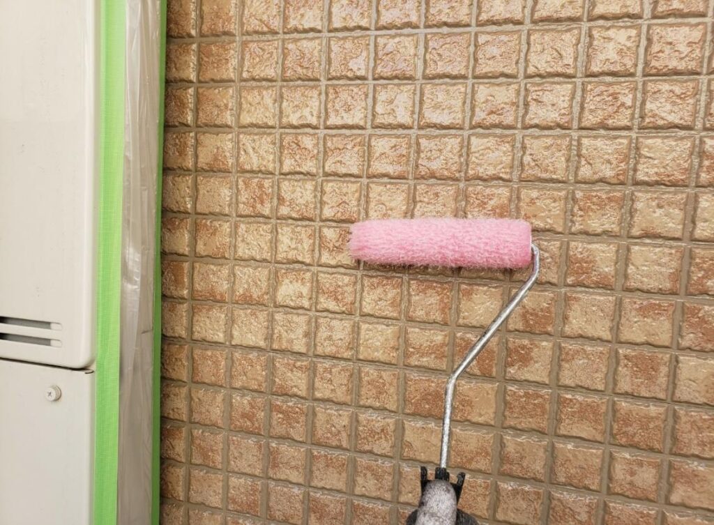 練馬区の集合住宅で、外壁クリヤー塗装の上塗り2回目として、塗膜の厚みと質感を整えながらローラーで仕上げ塗装を行っている様子