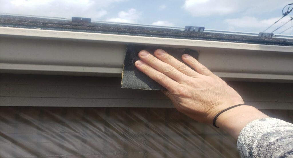 練馬区の集合住宅で、雨樋塗装工事に向けて既存塗膜を落とすためケレン作業を行っている様子