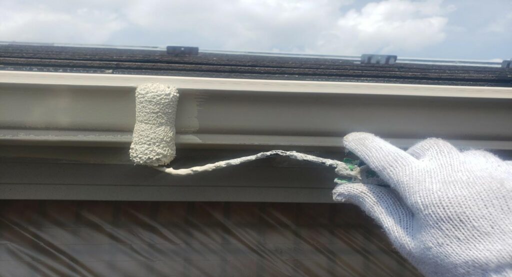 練馬区の集合住宅で、ケレン作業後の雨樋に中塗り塗装をローラーで施工している様子