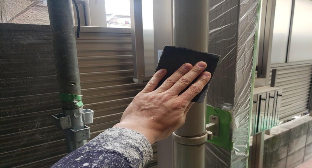 練馬区の集合住宅で、竪樋塗装工事に向けて塗装前の下地処理としてケレン作業を行っている様子