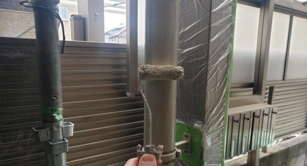 練馬区の集合住宅で、竪樋塗装工事の中塗りとしてローラーで塗料を塗布している施工中の様子
