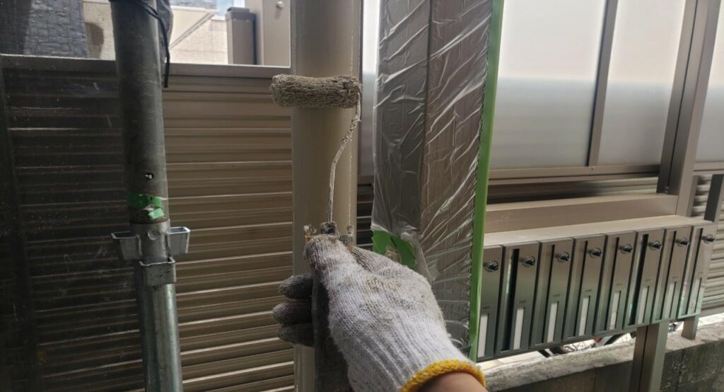 練馬区の集合住宅で、竪樋塗装工事の仕上げとして上塗り塗装をローラーで施工している作業中の様子