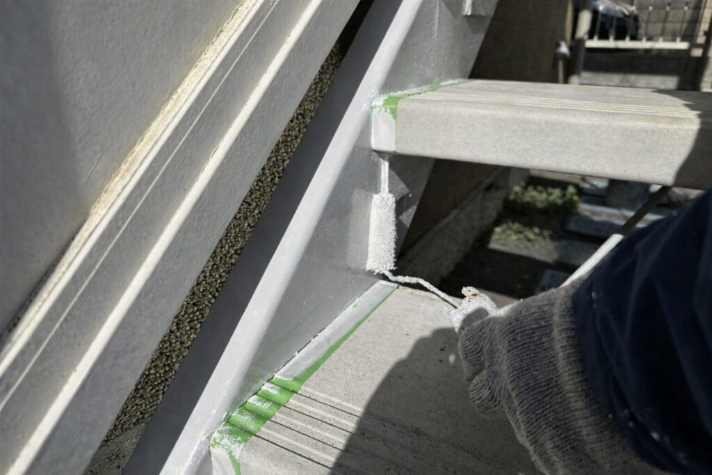 練馬区の集合住宅にある鉄骨階段ササラ取り合い部へ中塗り塗料を塗布している様子