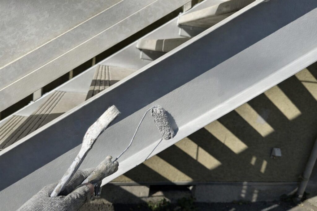 練馬区の集合住宅にある鉄骨階段ササラへ上塗り塗料をローラーで仕上げ施工している様子