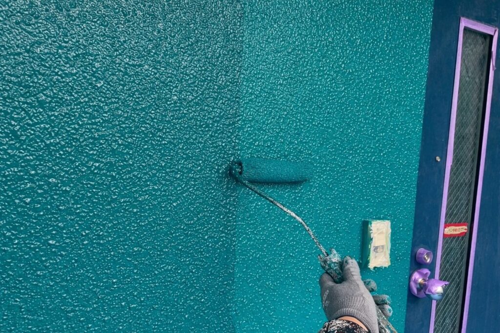 練馬区の集合住宅で吹付仕上げ外壁に仕上げ塗料の上塗りをローラーで施工している様子