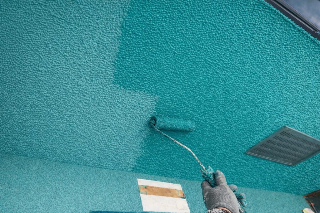 練馬区の集合住宅で吹付仕上げの軒裏天井に仕上げ塗料の上塗りをローラーで施工している様子