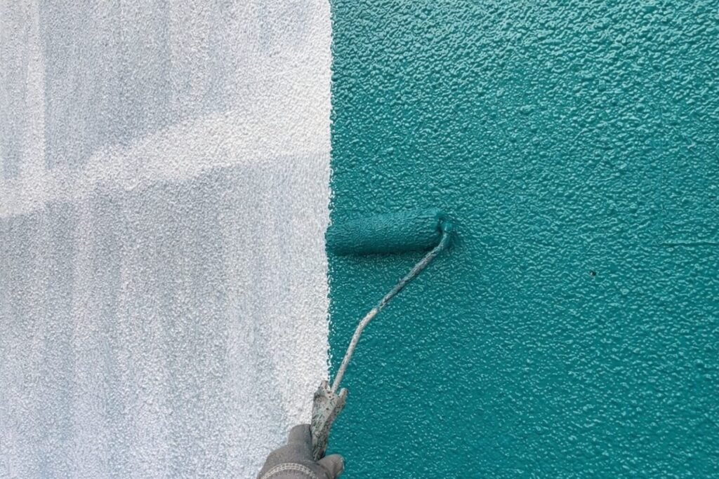 練馬区の集合住宅で外壁に仕上げ塗料の中塗りをローラーで施工している様子